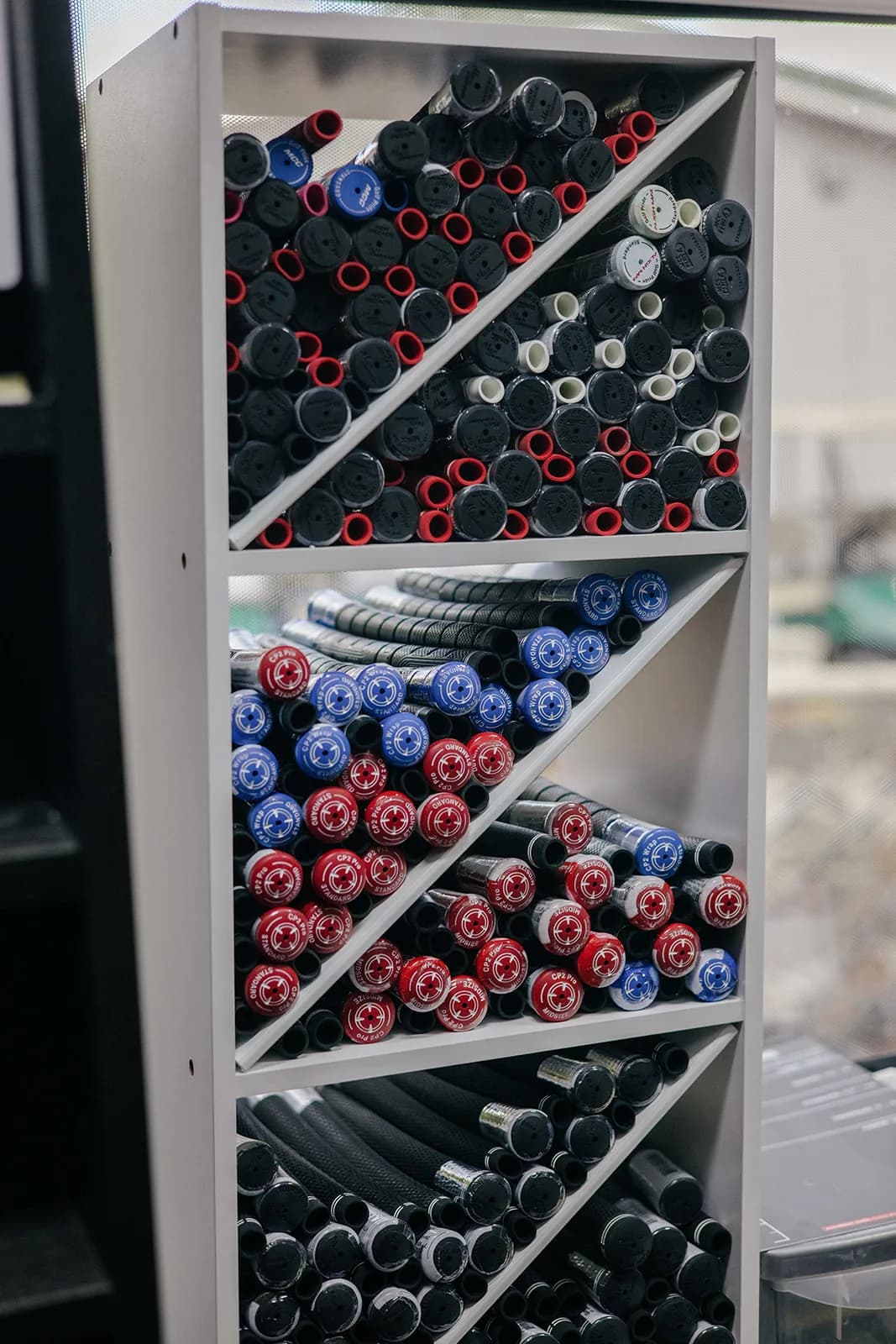 A rack of new grips in the workshop, Golf Pride among them, sorted on diagonal shelves