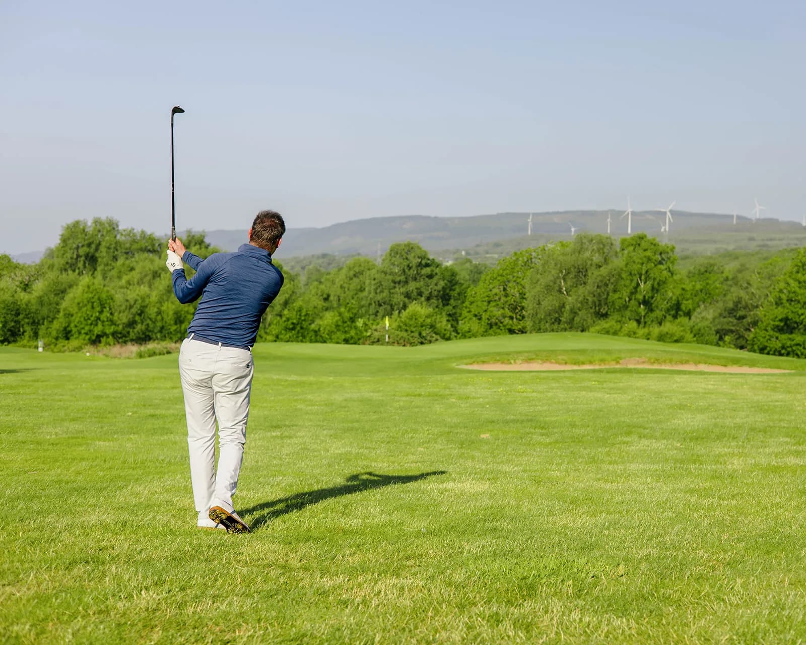 Stuart Wilson holding his finish after an approach to a bunkered green, with wind turbines on the hills behind
